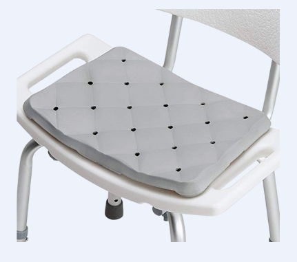 A gray seat cushion with holes for drainage sitting on top of a plastic shower chair.