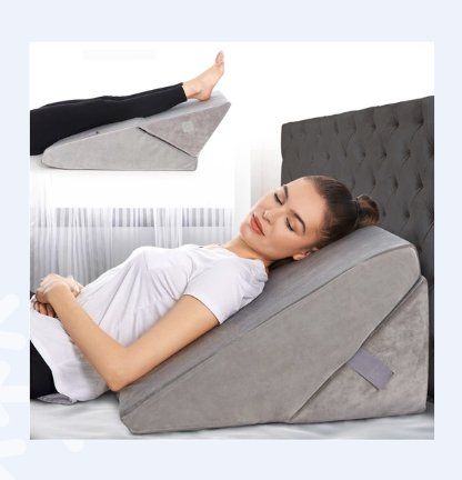 A woman resting on a gray wedge cushion with an image of elevated legs on the same gray wedge cushion in the upper corner.
