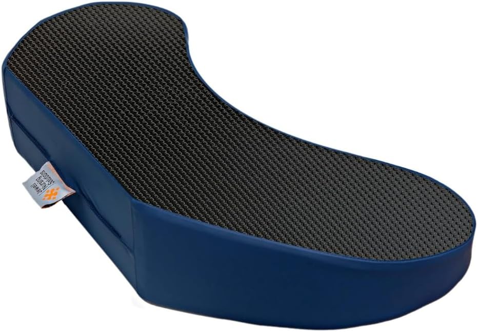 The image displays an ergonomically designed bedsore prevention pillow called Bedsore Rescue by Jewell Nursing Solutions. It has a unique contoured shape, wider at one end and tapering at the other. The pillow is covered in a non-skid, textured fabric on the top surface and has a solid navy blue color on the sides. A visible label with the Bedsore Rescue logo is attached to the side, indicating the brand. This type of pillow is typically used to relieve pressure and prevent bedsores for individuals confined to lying in bed for extended periods.