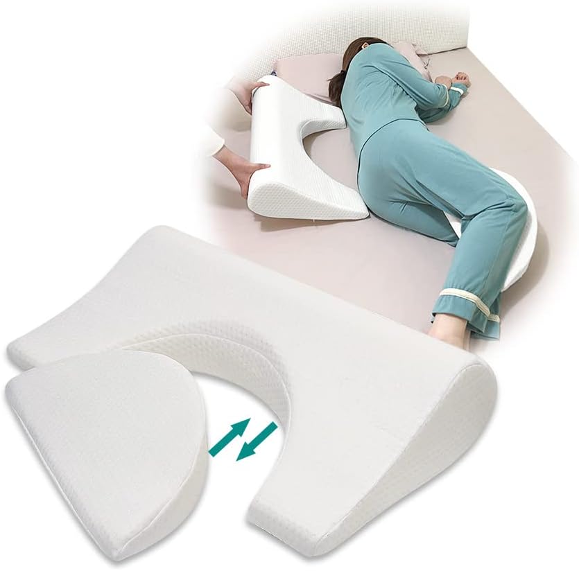 An image showcasing a specialty bed pillow designed to prevent and treat bedsores. The pillow is white and shaped in a unique contoured form with a cutout area in the center. It is shown in use: a person lying on their side on a bed, with the pillow placed between their knees to alleviate pressure. The person is wearing teal pajamas, and only their body from the neck down is visible, highlighting the positioning of the pillow. An arrow graphic points to the space created by the pillow's design, indicating the area intended to reduce pressure on the body.